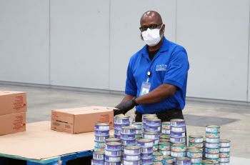 Man wearing mask standing at table with donated cans