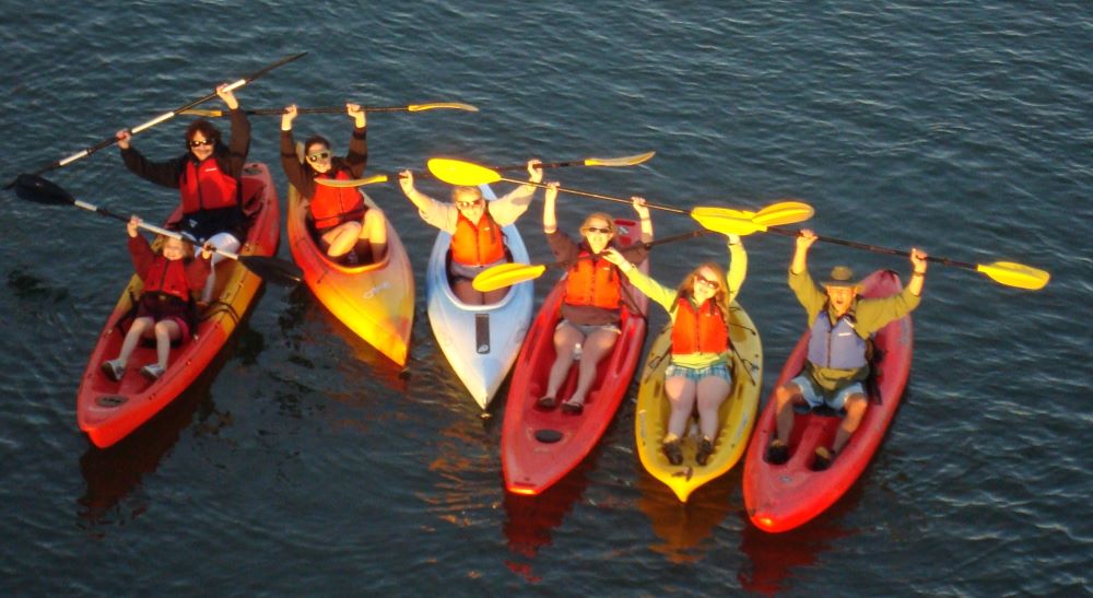 Group holding up paddles while in kayaks